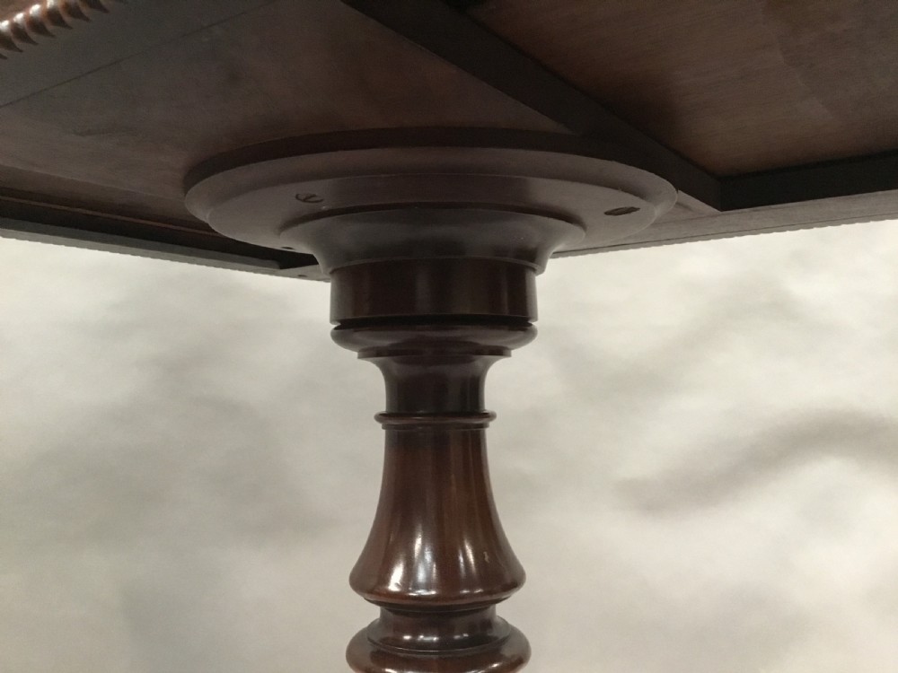 A Regency mahogany writing table featuring an adjustable hinged top, a single drawer with turned knobs, a turned central pedestal, and reeded tripod legs ending in brass castors. View XX