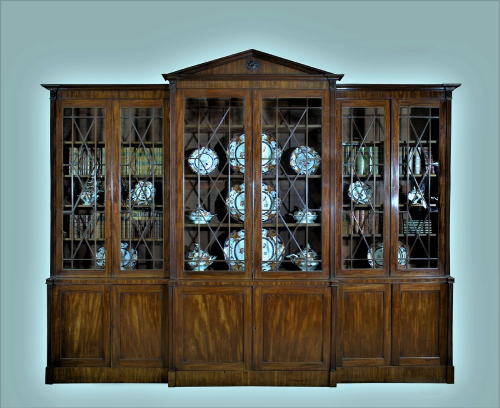 A large George III mahogany breakfront bookcase with a central pediment, glazed upper doors with geometric glazing bars, and flame mahogany cupboard doors below.