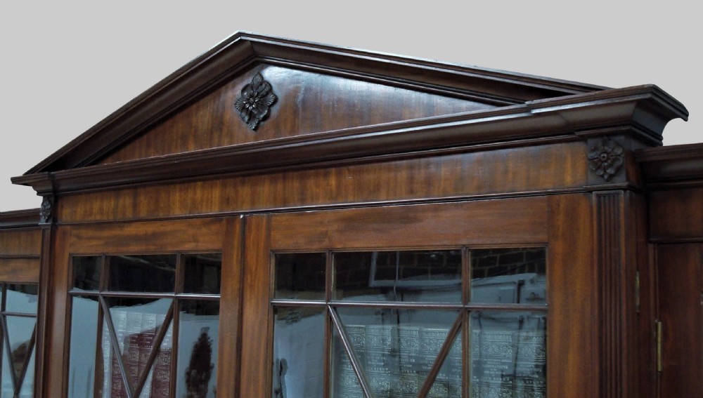 A large George III mahogany breakfront bookcase with a central pediment, glazed upper doors with geometric glazing bars, and flame mahogany cupboard doors below. View IV