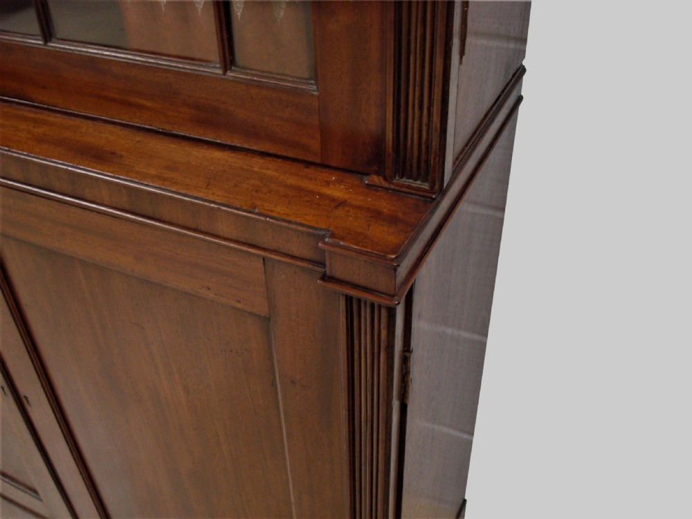 A large George III mahogany breakfront bookcase with a central pediment, glazed upper doors with geometric glazing bars, and flame mahogany cupboard doors below. View VI