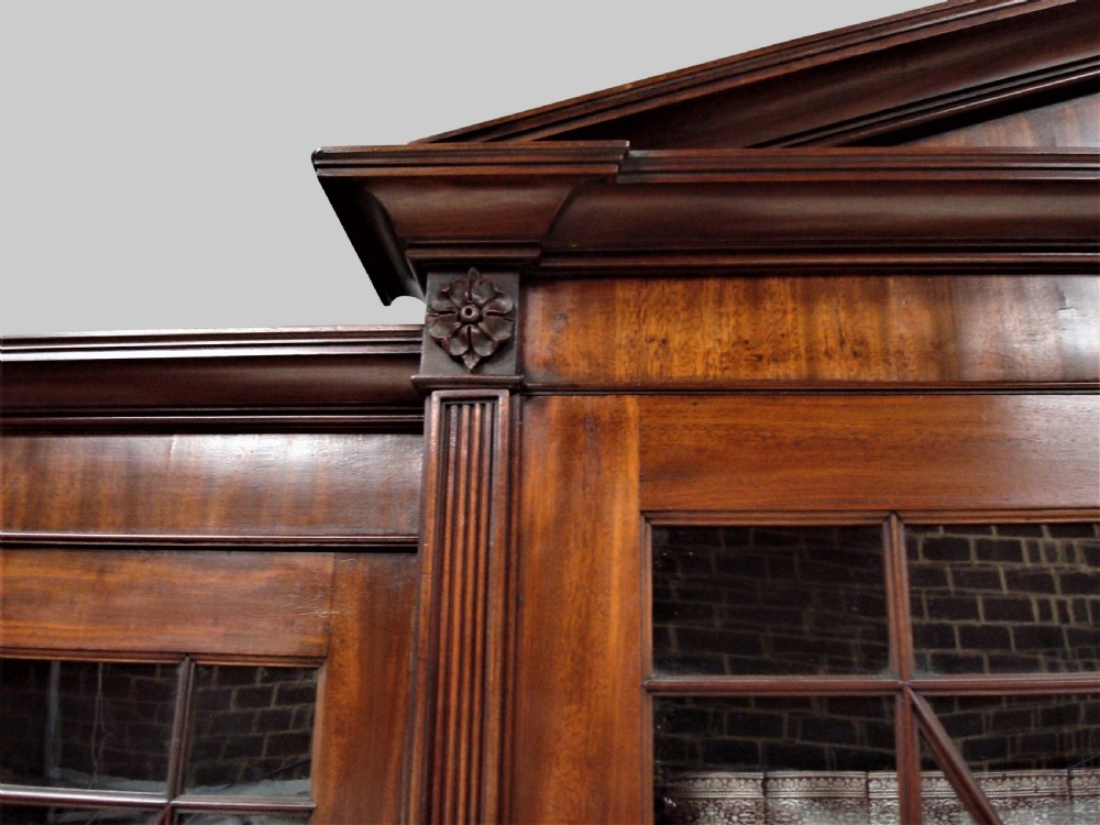 A large George III mahogany breakfront bookcase with a central pediment, glazed upper doors with geometric glazing bars, and flame mahogany cupboard doors below. View VII