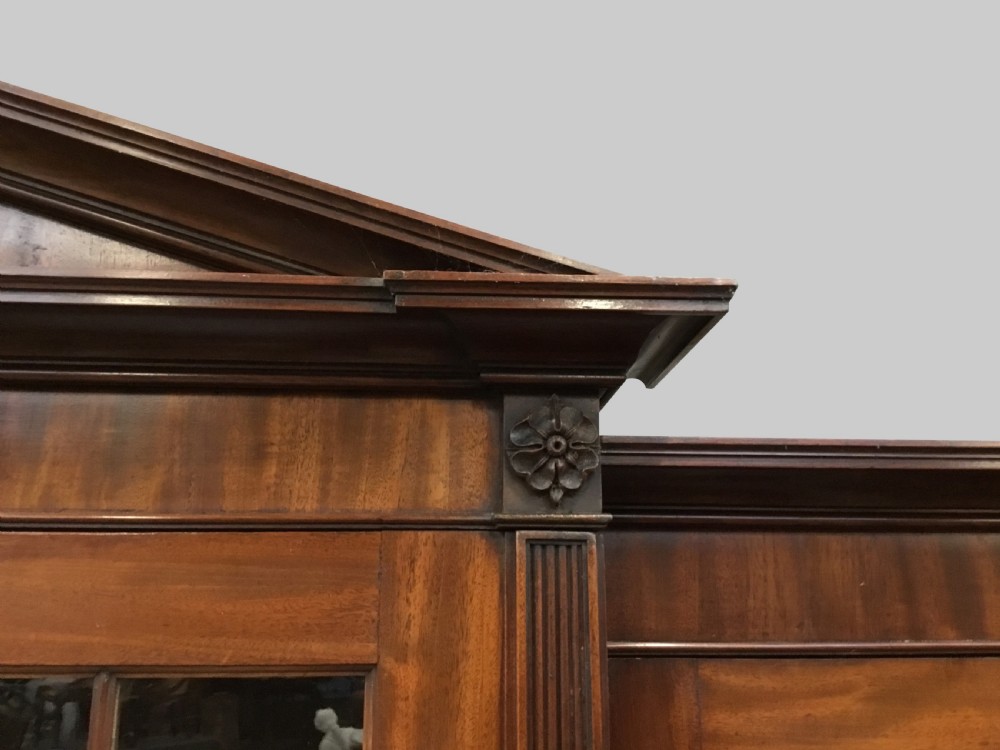 A large George III mahogany breakfront bookcase with a central pediment, glazed upper doors with geometric glazing bars, and flame mahogany cupboard doors below. View IX