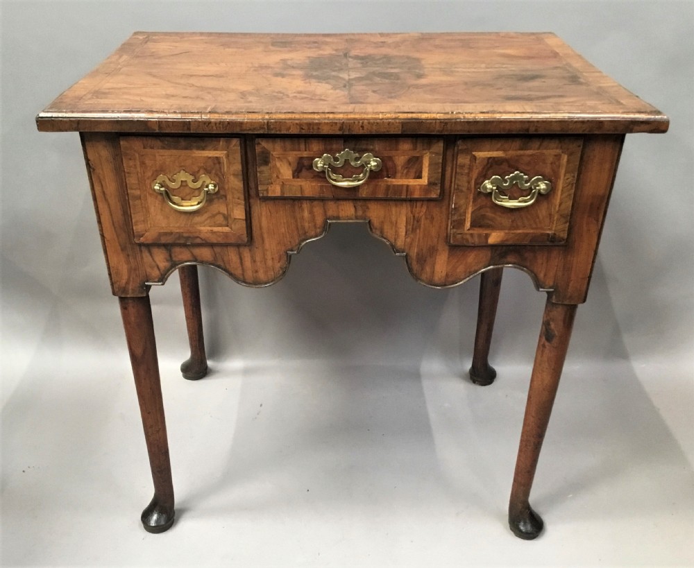 An 18th-century George I figured walnut lowboy with three drawers, brass handles, a shaped apron, and slender cabriole legs with pad feet.
