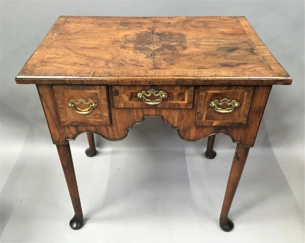 An 18th-century George I figured walnut lowboy with three drawers, brass handles, a shaped apron, and slender cabriole legs with pad feet. View II