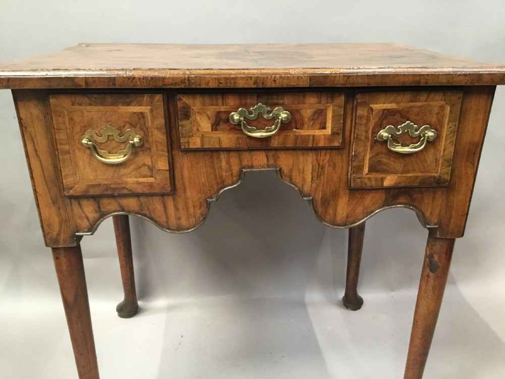 An 18th-century George I figured walnut lowboy with three drawers, brass handles, a shaped apron, and slender cabriole legs with pad feet. View V