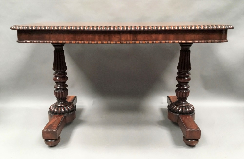 A Regency mahogany library table featuring a carved gadrooned border, reeded turned legs, and a trestle base with feet. View V