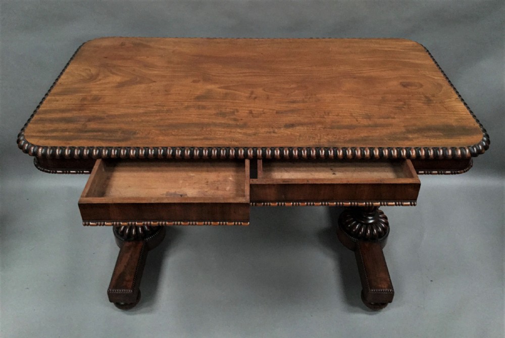 A Regency mahogany library table featuring a carved gadrooned border, reeded turned legs, and a trestle base with feet. View X