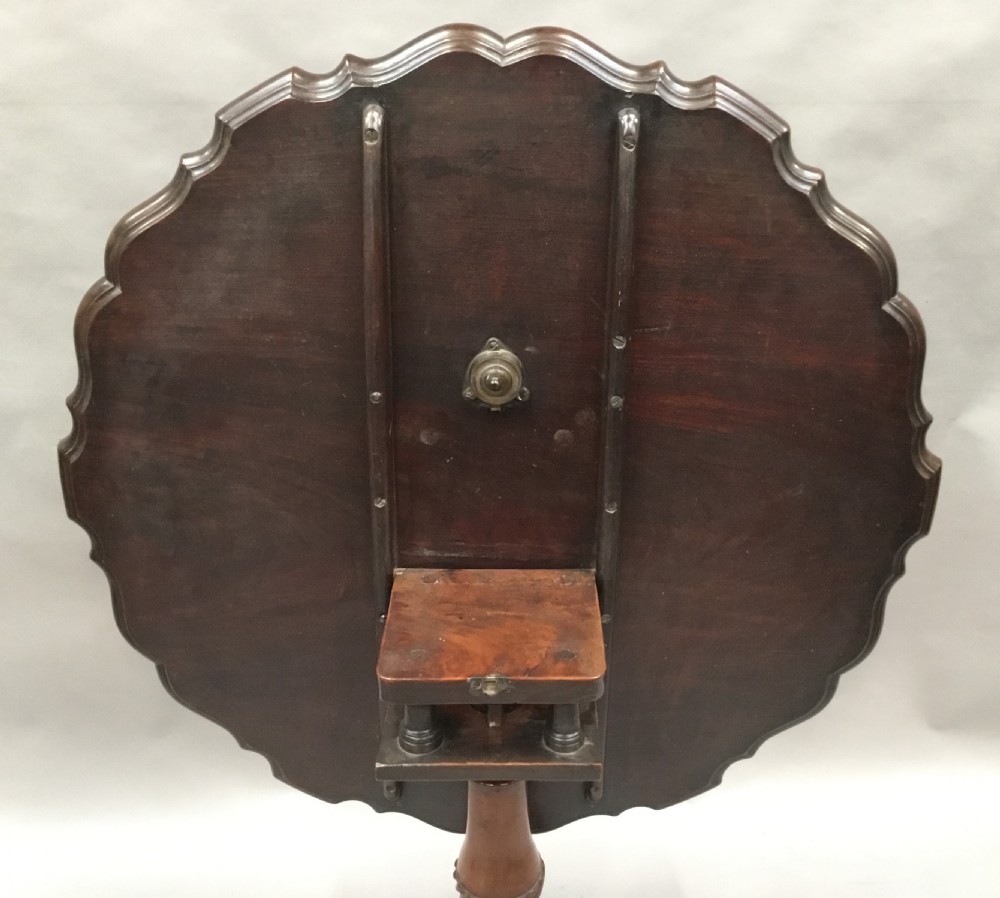 A mahogany George III style tripod table featuring a scalloped piecrust top, turned pedestal column, and cabriole legs with carved feet. View XXI