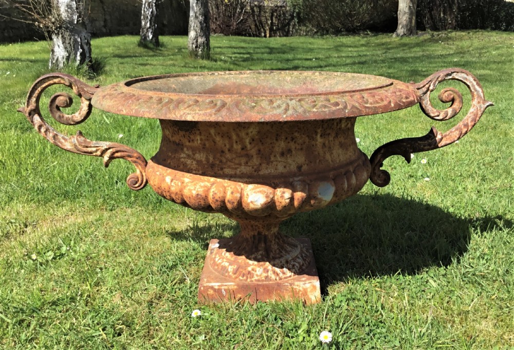A pair of weathered 19th-century cast iron garden urns of shallow campana form with large scroll handles and square pedestal bases. View IV