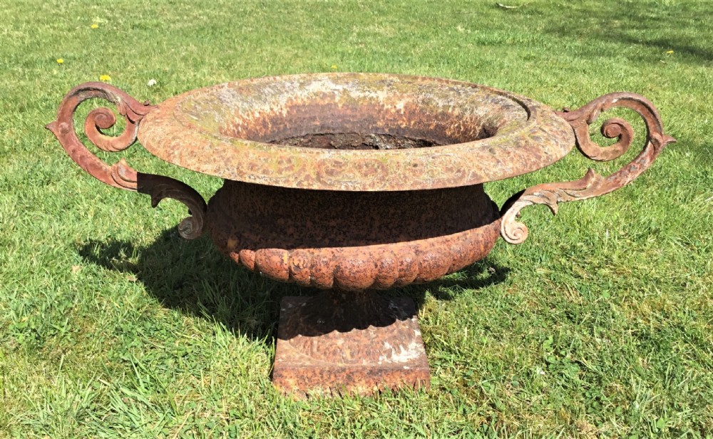 A pair of weathered 19th-century cast iron garden urns of shallow campana form with large scroll handles and square pedestal bases. View V