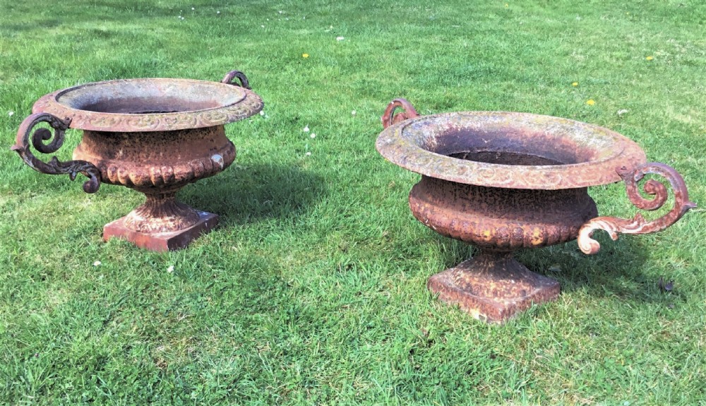 A pair of weathered 19th-century cast iron garden urns of shallow campana form with large scroll handles and square pedestal bases. View X