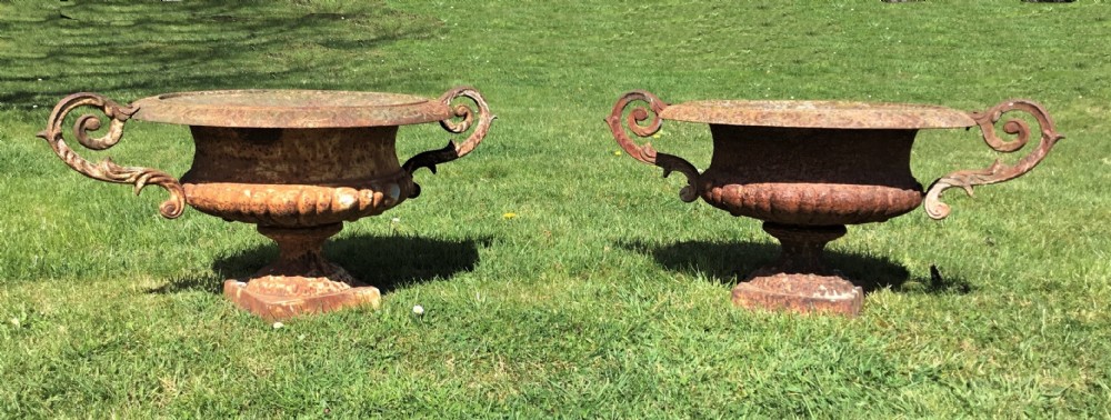 A pair of weathered 19th-century cast iron garden urns of shallow campana form with large scroll handles and square pedestal bases.