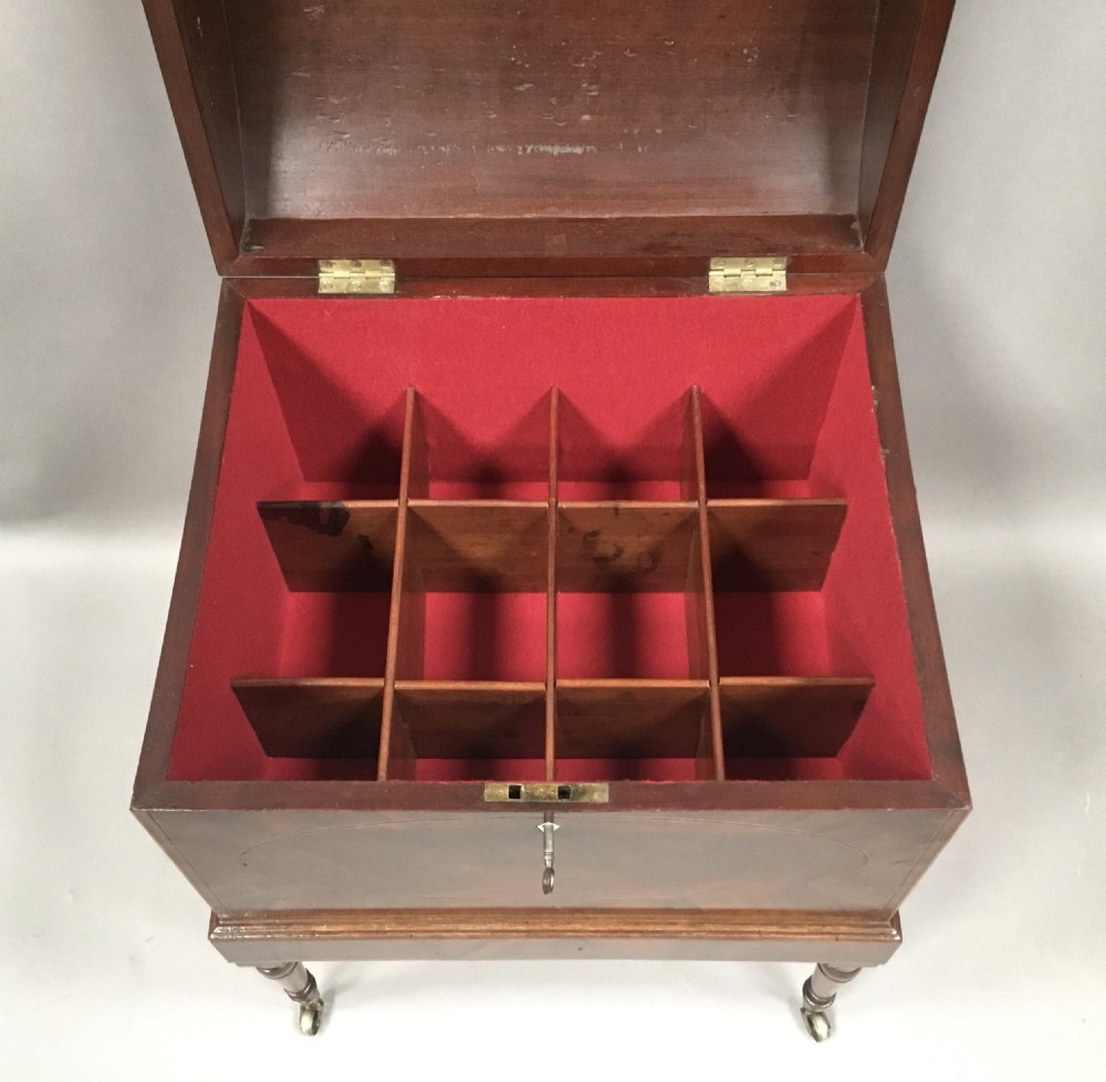 A George III Sheraton style flame mahogany cellarette featuring a domed lid, oval stringing inlay, brass side handles, and turned legs on castors. View VI