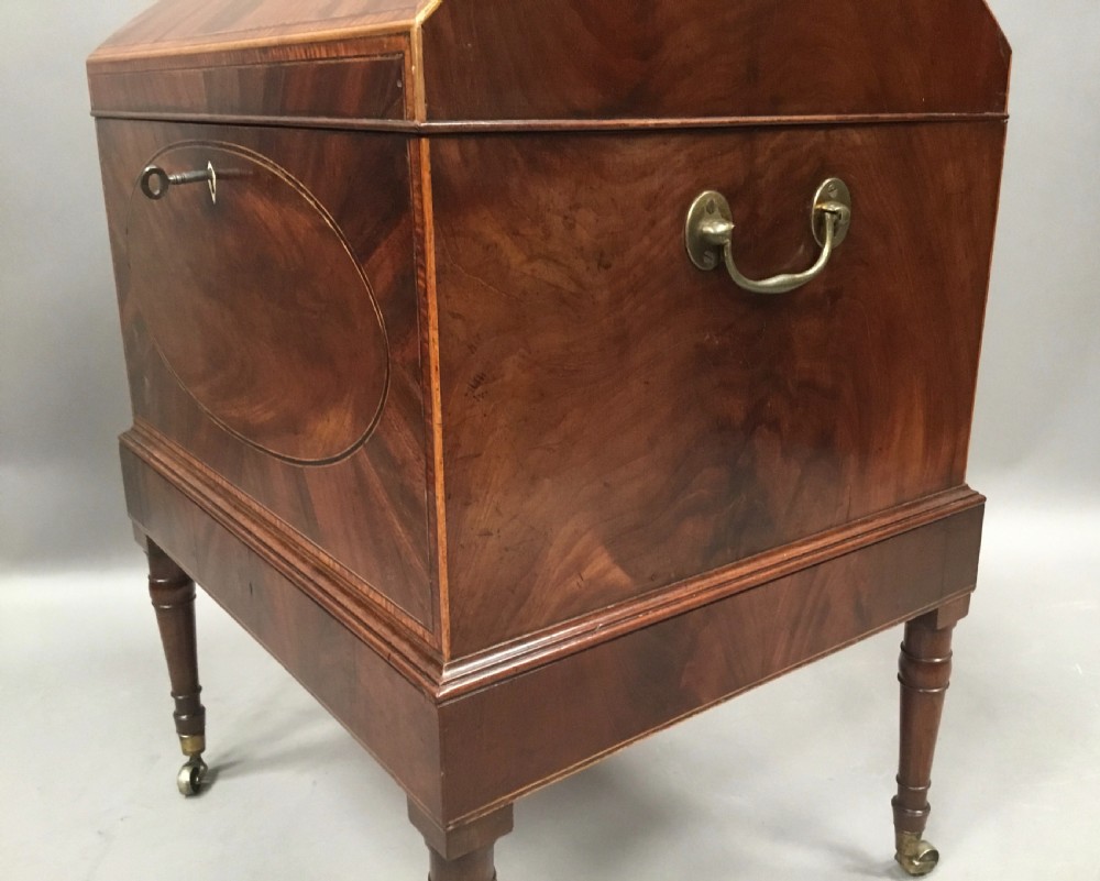 A George III Sheraton style flame mahogany cellarette featuring a domed lid, oval stringing inlay, brass side handles, and turned legs on castors. View VIII