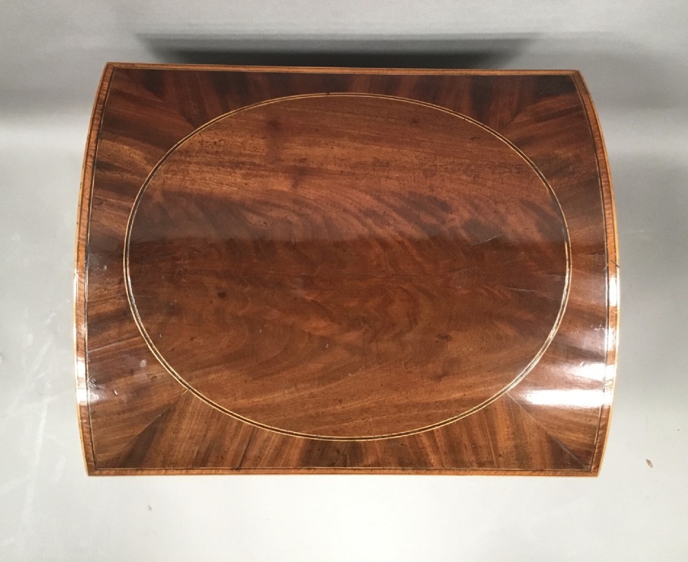 A George III Sheraton style flame mahogany cellarette featuring a domed lid, oval stringing inlay, brass side handles, and turned legs on castors. View X