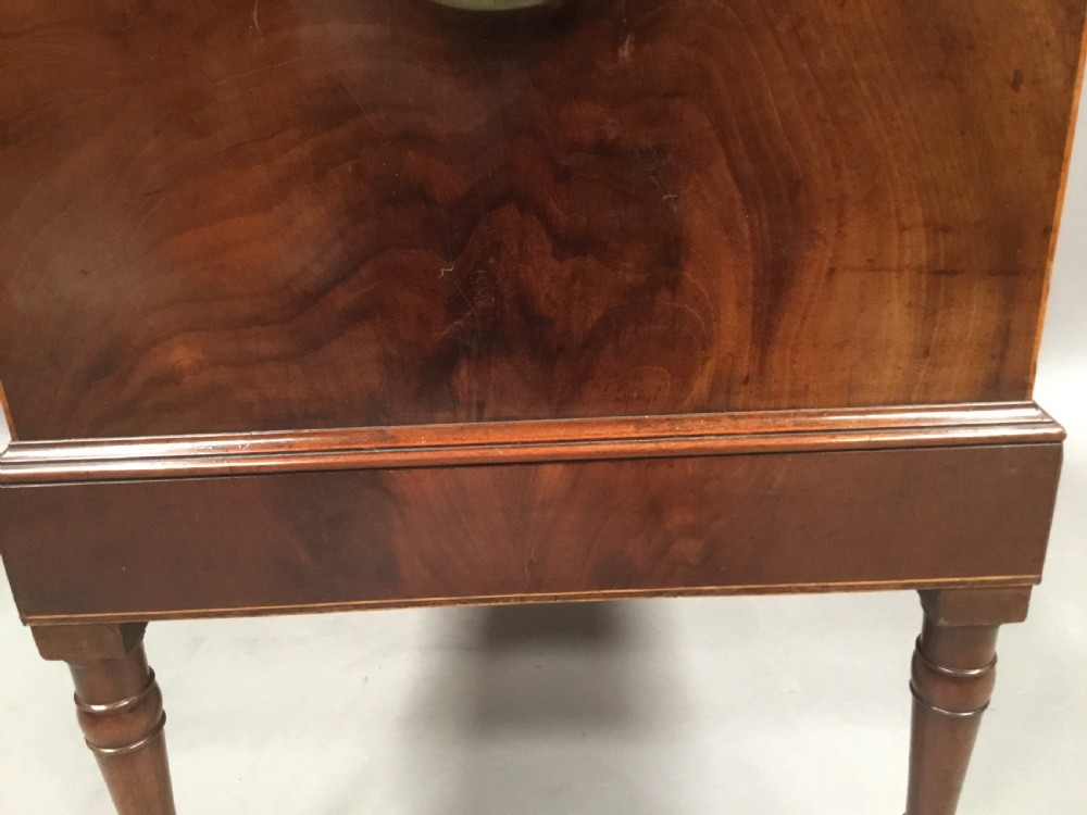 A George III Sheraton style flame mahogany cellarette featuring a domed lid, oval stringing inlay, brass side handles, and turned legs on castors. View XIX