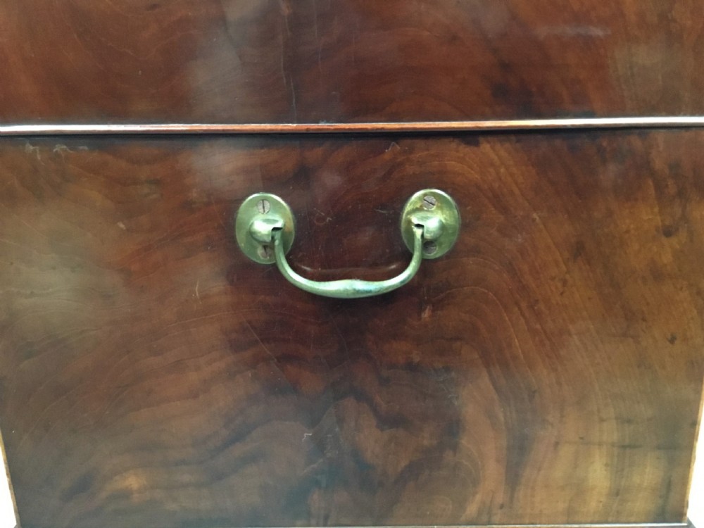 A George III Sheraton style flame mahogany cellarette featuring a domed lid, oval stringing inlay, brass side handles, and turned legs on castors. View XX