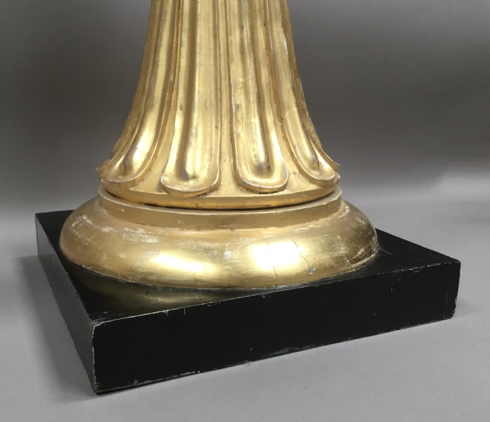 A pair of tall Regency Neoclassical giltwood torchere stands featuring fluted stems, decorative leaf moulding, and square black plinths. View XX
