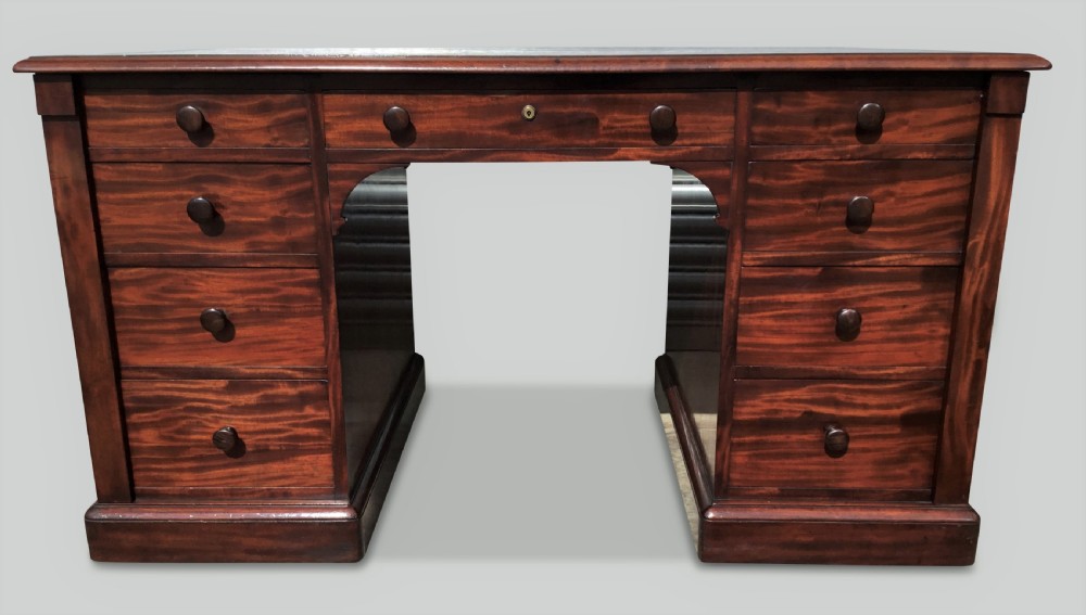 A Regency flame mahogany pedestal desk with an inset brown leather top, multiple drawers with turned wooden knobs, and twin panelled pedestals. View IV