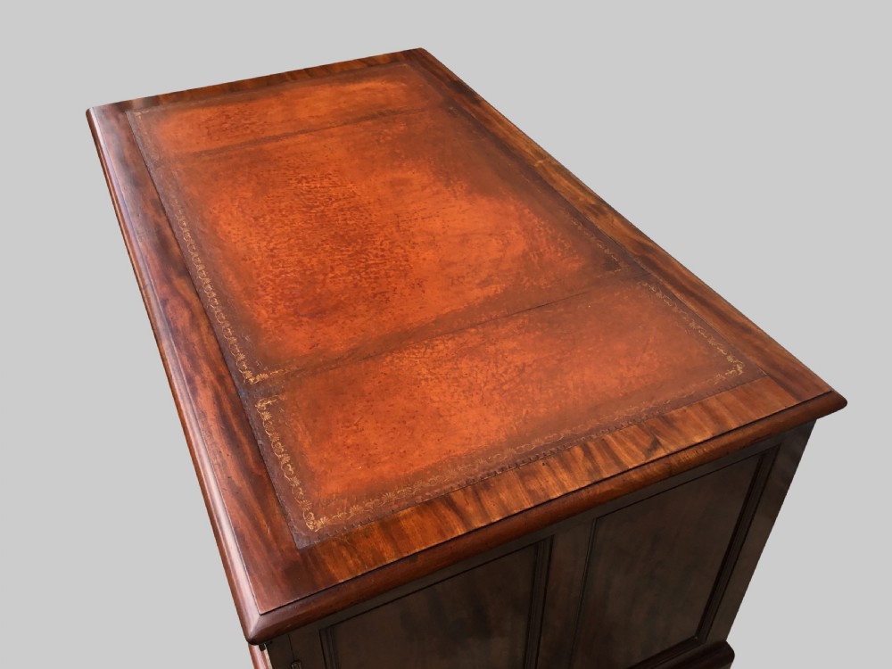 A Regency flame mahogany pedestal desk with an inset brown leather top, multiple drawers with turned wooden knobs, and twin panelled pedestals. View V