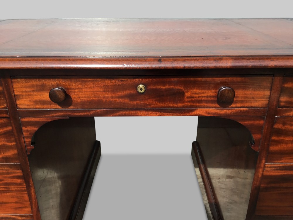 A Regency flame mahogany pedestal desk with an inset brown leather top, multiple drawers with turned wooden knobs, and twin panelled pedestals. View XVII