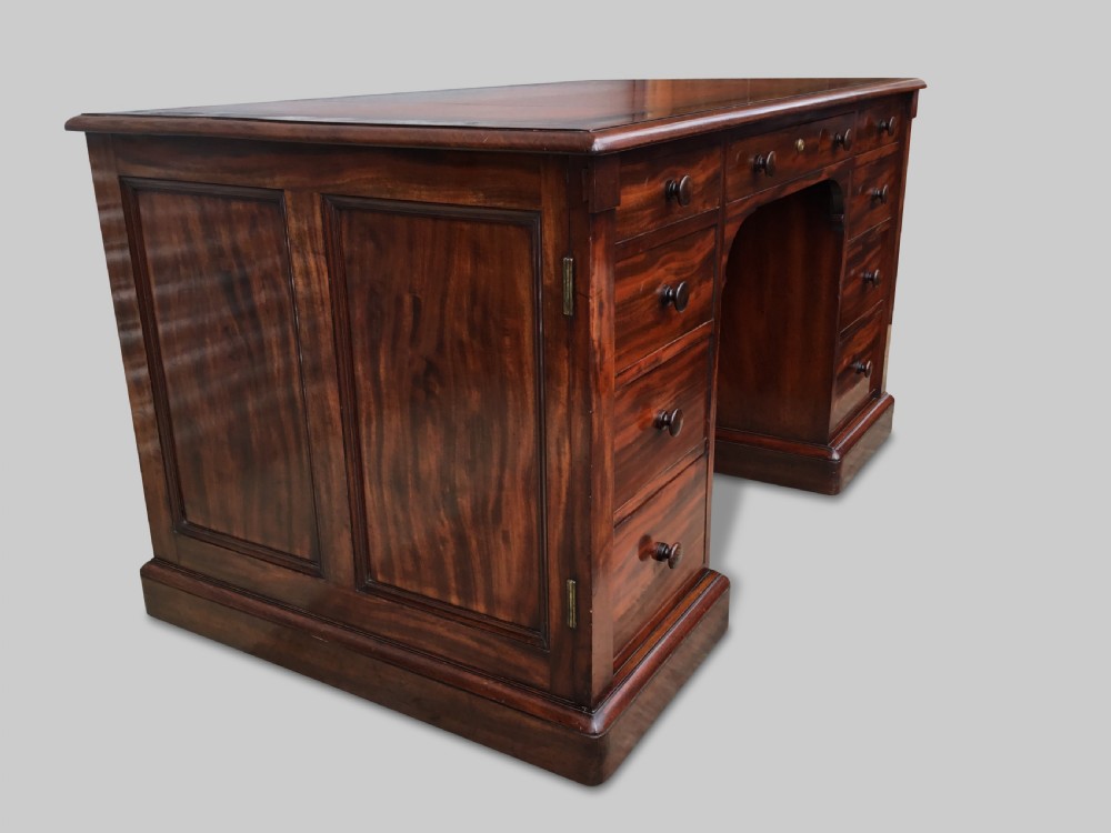 A Regency flame mahogany pedestal desk with an inset brown leather top, multiple drawers with turned wooden knobs, and twin panelled pedestals. View XXI