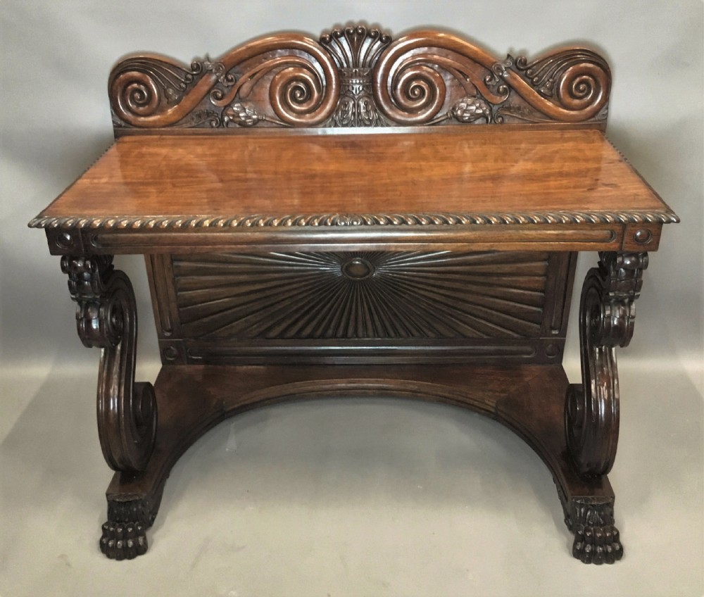 A 19th-century carved padouk console table featuring S-scroll legs, paw feet, a sunburst carved back panel, and a scrollwork gallery upstand. View IX