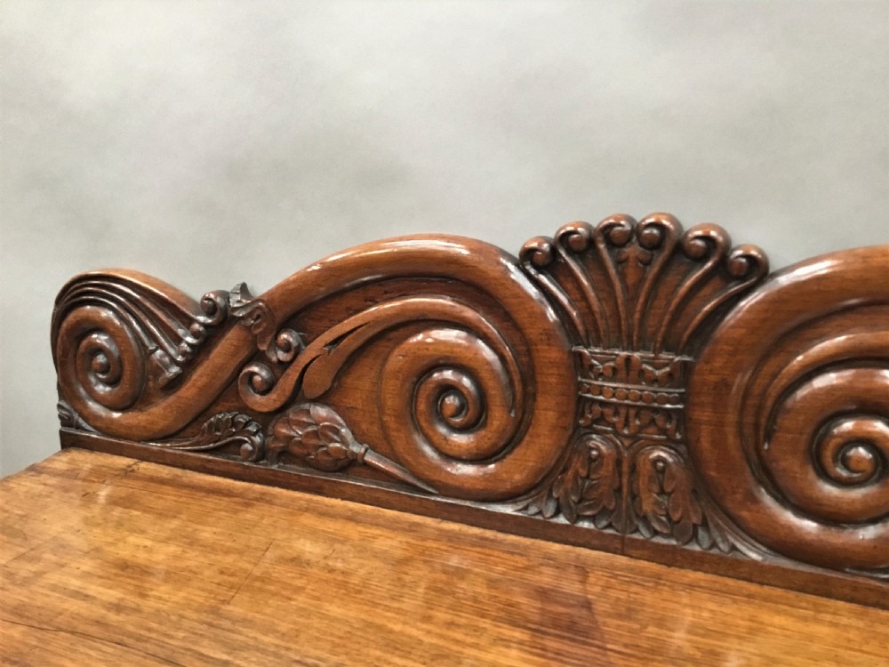 A 19th-century carved padouk console table featuring S-scroll legs, paw feet, a sunburst carved back panel, and a scrollwork gallery upstand. View XIX