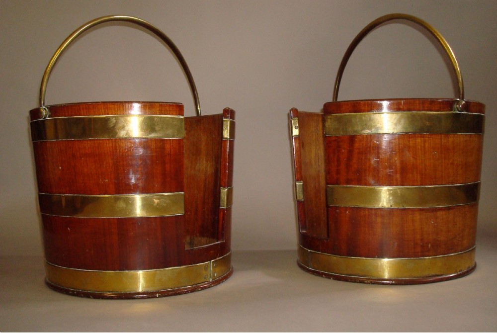 A pair of 18th-century mahogany plate buckets featuring brass binding straps, swing handles, and a vertical front cutout.