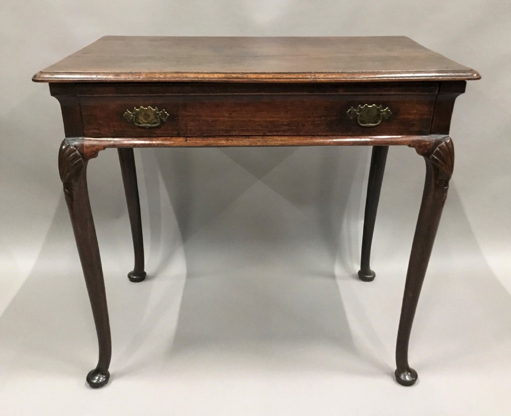 A George II dark walnut side table featuring carved shell knees on slender cabriole legs with pad feet and a single drawer with brass handles.