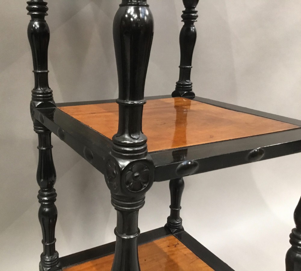 A four-tiered Ceylonese etagere featuring dark turned ebony supports and light satinwood shelf surfaces terminating in brass castors. View V