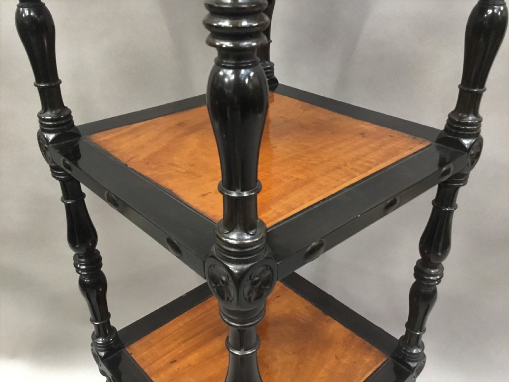 A four-tiered Ceylonese etagere featuring dark turned ebony supports and light satinwood shelf surfaces terminating in brass castors. View XII
