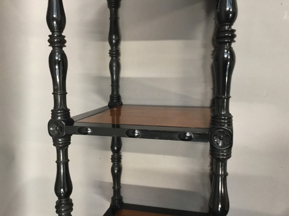 A four-tiered Ceylonese etagere featuring dark turned ebony supports and light satinwood shelf surfaces terminating in brass castors. View XXI