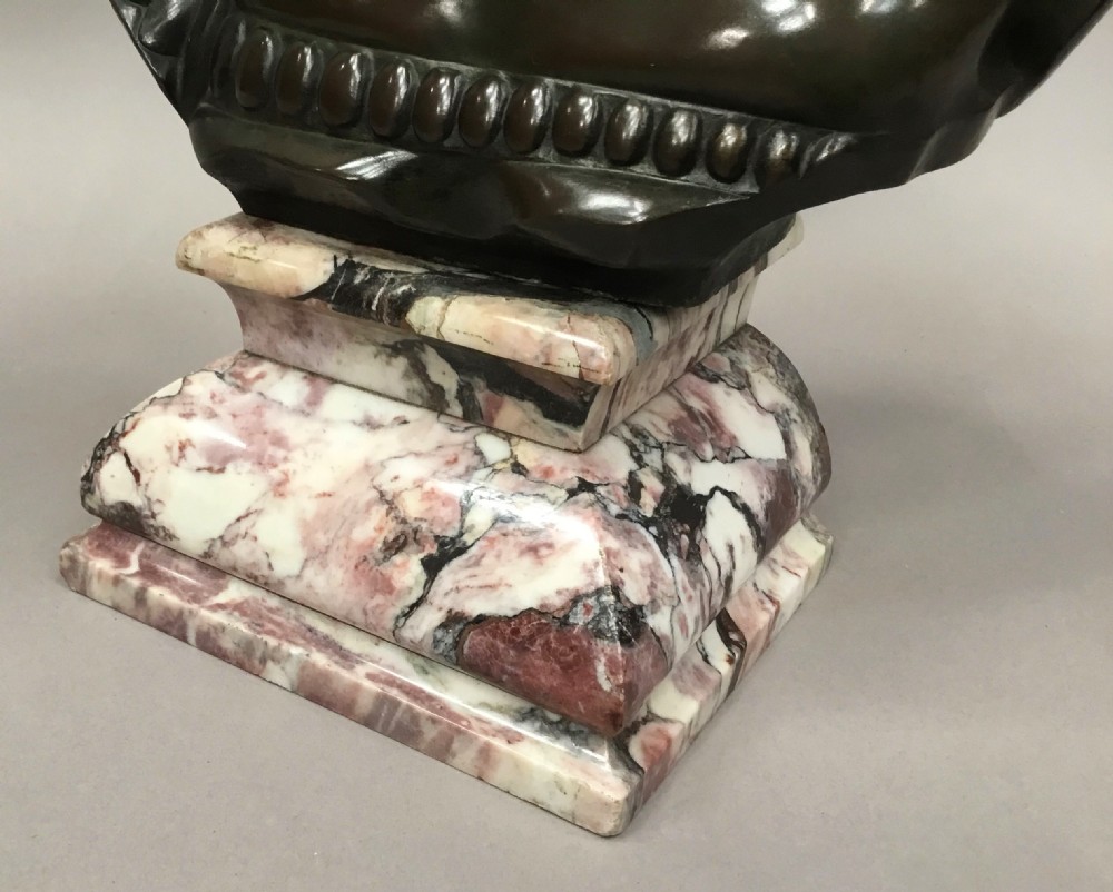 A 19th-century dark bronze bust depicting a helmeted Roman gladiator with a beard, mounted on a square variegated pink marble base. View IX