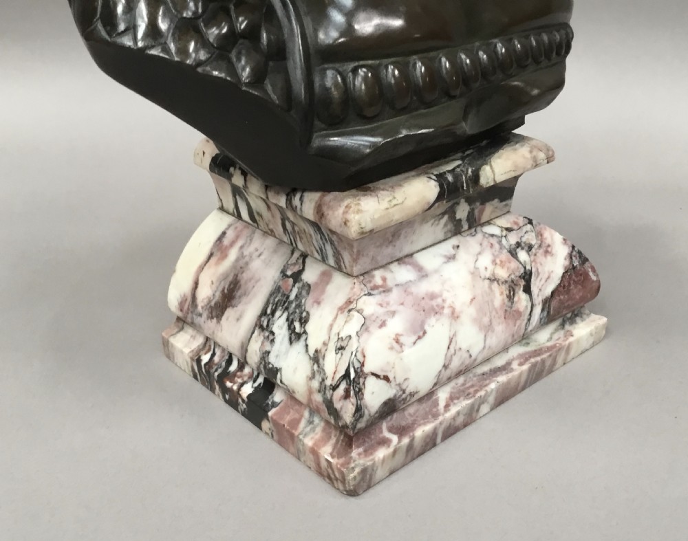 A 19th-century dark bronze bust depicting a helmeted Roman gladiator with a beard, mounted on a square variegated pink marble base. View XIX