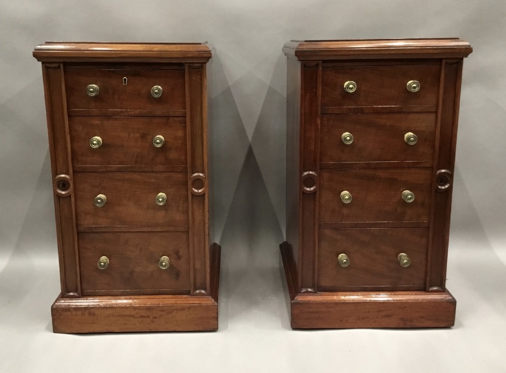 A pair of tall, narrow mahogany Wellington chests featuring four drawers each, turned brass knobs, and carved roundel pilasters on plinth bases.