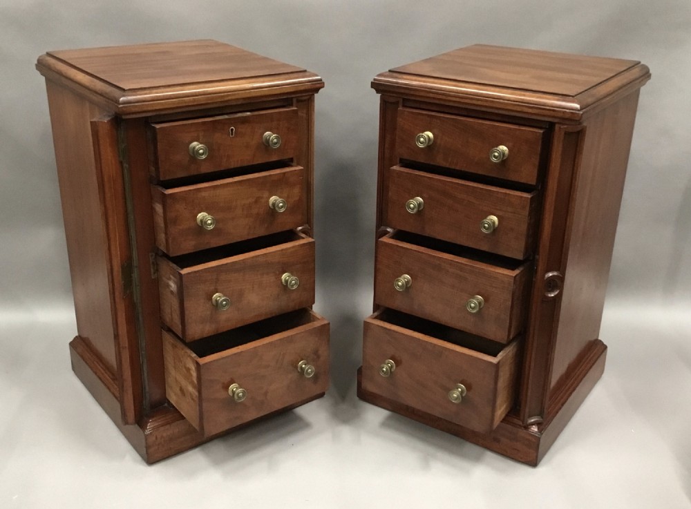 A pair of tall, narrow mahogany Wellington chests featuring four drawers each, turned brass knobs, and carved roundel pilasters on plinth bases. View V