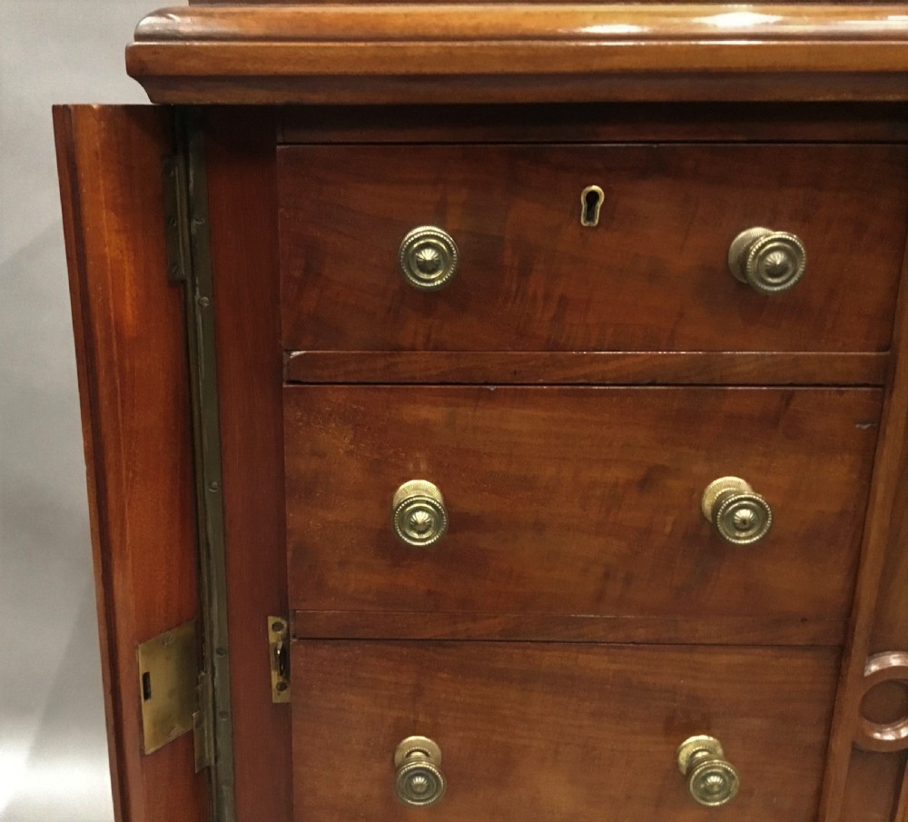 A pair of tall, narrow mahogany Wellington chests featuring four drawers each, turned brass knobs, and carved roundel pilasters on plinth bases. View IX