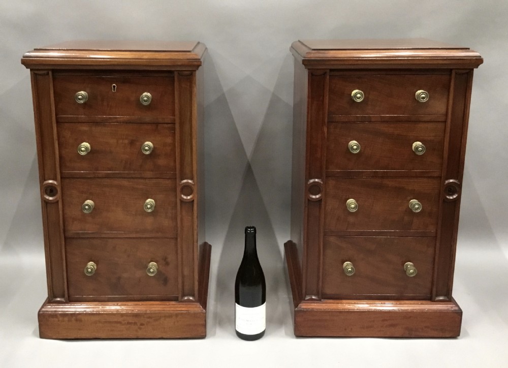 A pair of tall, narrow mahogany Wellington chests featuring four drawers each, turned brass knobs, and carved roundel pilasters on plinth bases. View XVII