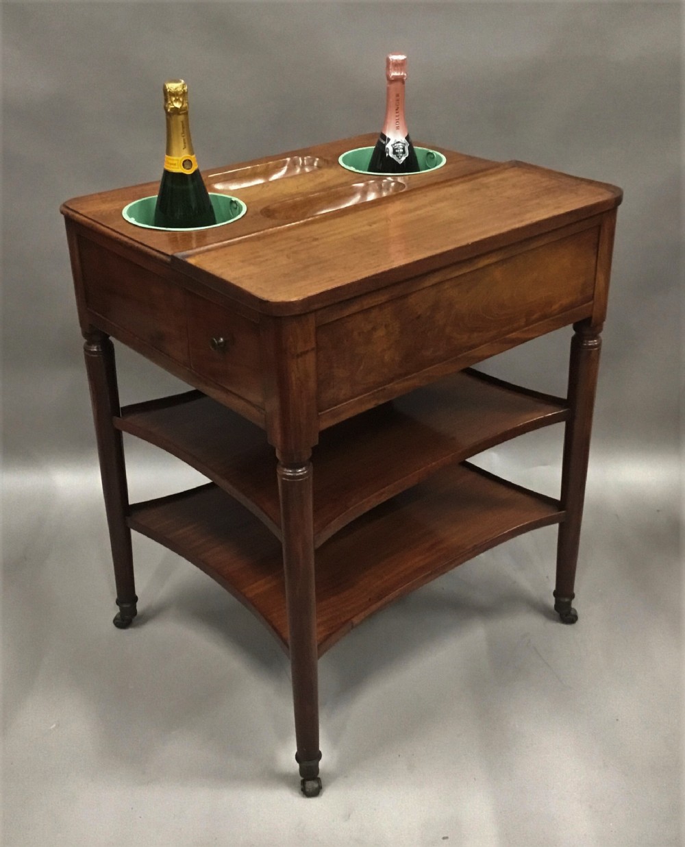 A French Louis XVI style mahogany rafraichissoir wine table with two inset metal bottle coolers, lower tiered shelves, and turned fluted legs on castors.