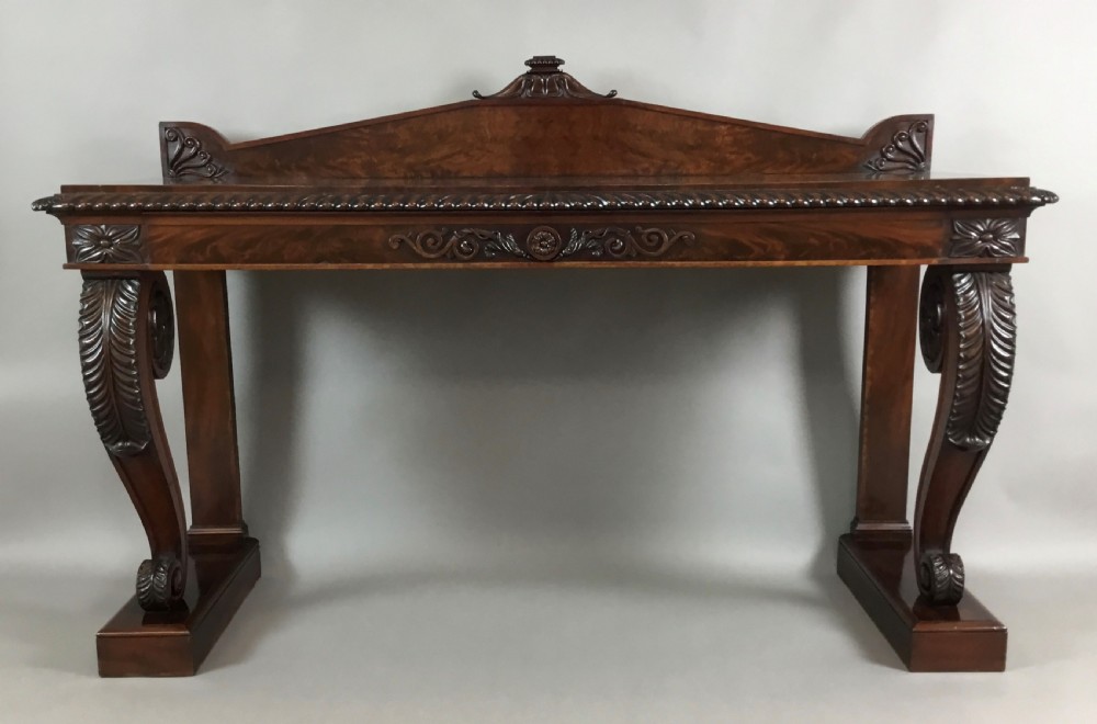 A Regency period dark mahogany serving table featuring carved scroll legs with acanthus leaves, a gadrooned top edge, and a raised carved backrail.