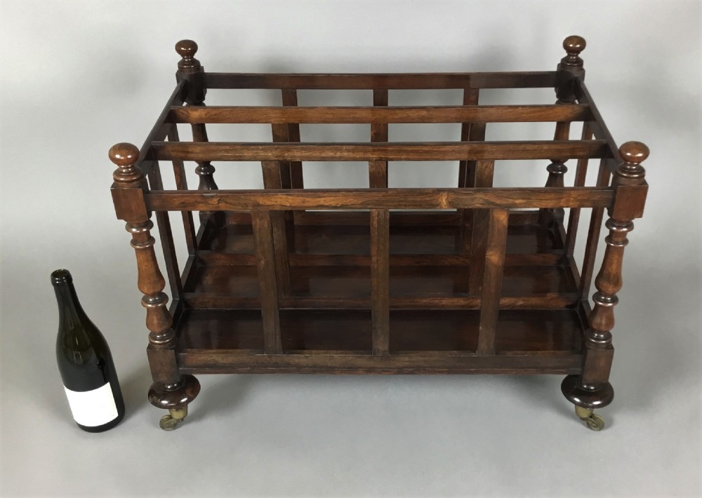A dark rosewood Regency folio stand featuring slatted partitions, turned corner posts topped with finials, and brass wheel castors. View III