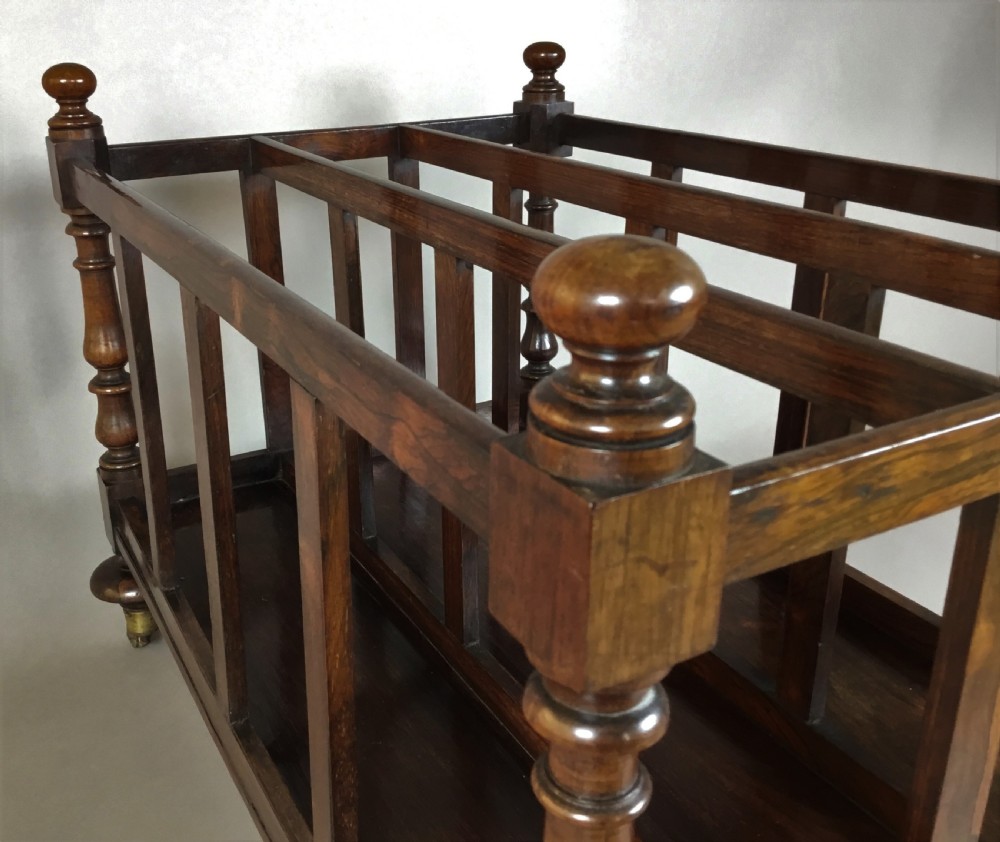 A dark rosewood Regency folio stand featuring slatted partitions, turned corner posts topped with finials, and brass wheel castors. View IV