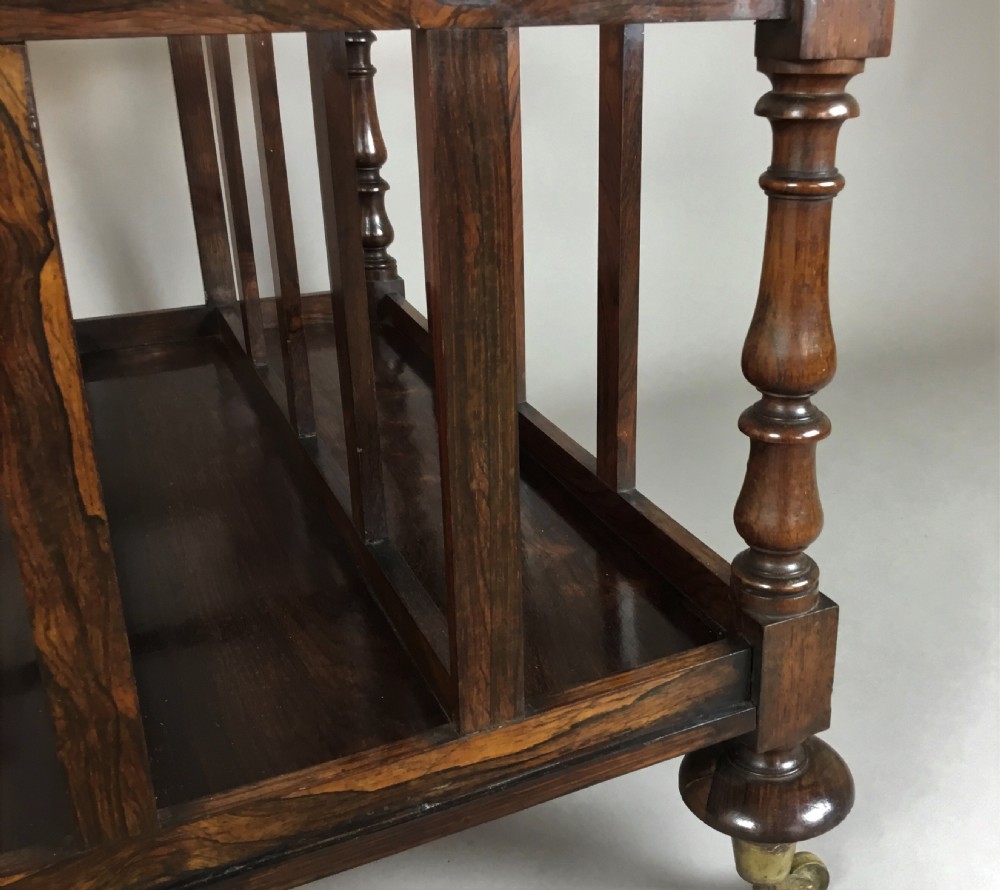 A dark rosewood Regency folio stand featuring slatted partitions, turned corner posts topped with finials, and brass wheel castors. View VII
