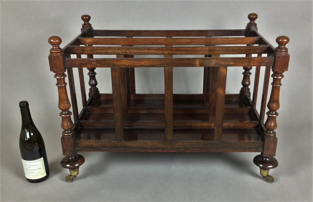 A dark rosewood Regency folio stand featuring slatted partitions, turned corner posts topped with finials, and brass wheel castors. View XII