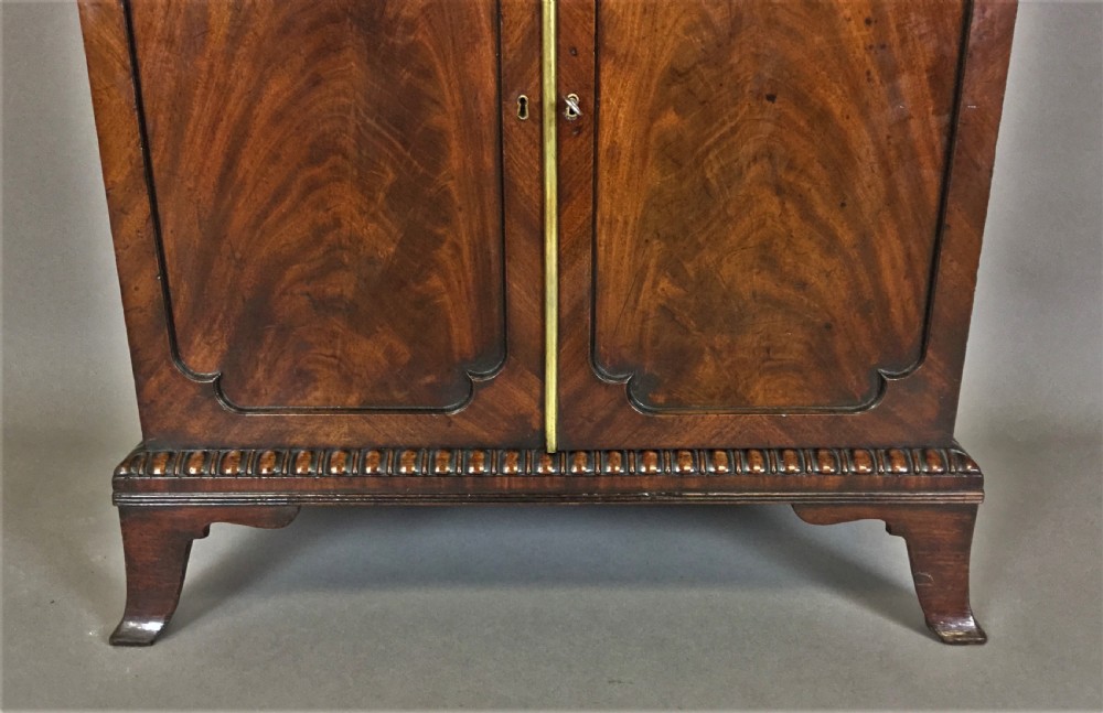 A Regency period mahogany secretaire cabinet featuring flame mahogany veneered doors with re-entrant corners, gadrooned borders, and bracket feet. View III