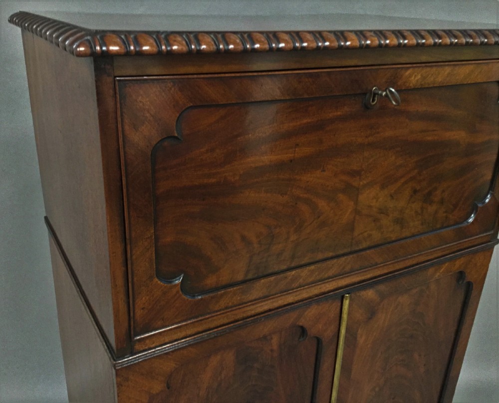 A Regency period mahogany secretaire cabinet featuring flame mahogany veneered doors with re-entrant corners, gadrooned borders, and bracket feet. View IV