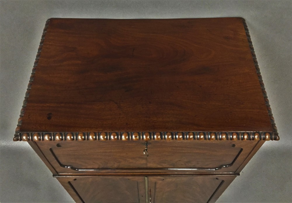 A Regency period mahogany secretaire cabinet featuring flame mahogany veneered doors with re-entrant corners, gadrooned borders, and bracket feet. View VI