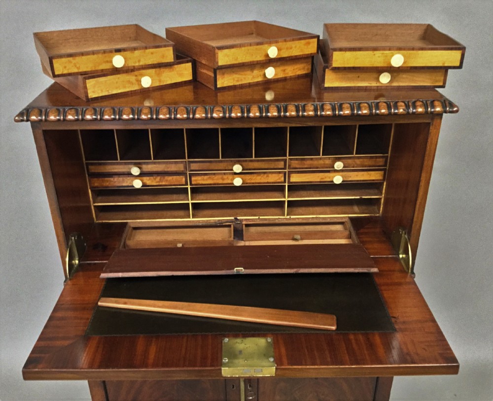 A Regency period mahogany secretaire cabinet featuring flame mahogany veneered doors with re-entrant corners, gadrooned borders, and bracket feet. View VII