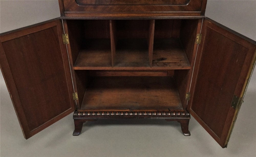 A Regency period mahogany secretaire cabinet featuring flame mahogany veneered doors with re-entrant corners, gadrooned borders, and bracket feet. View XII